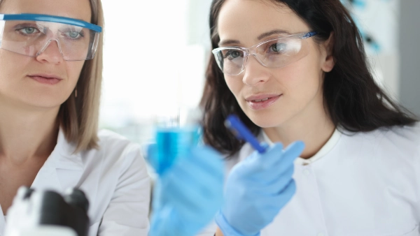 Two women with safety glasses analyzing blue liquid