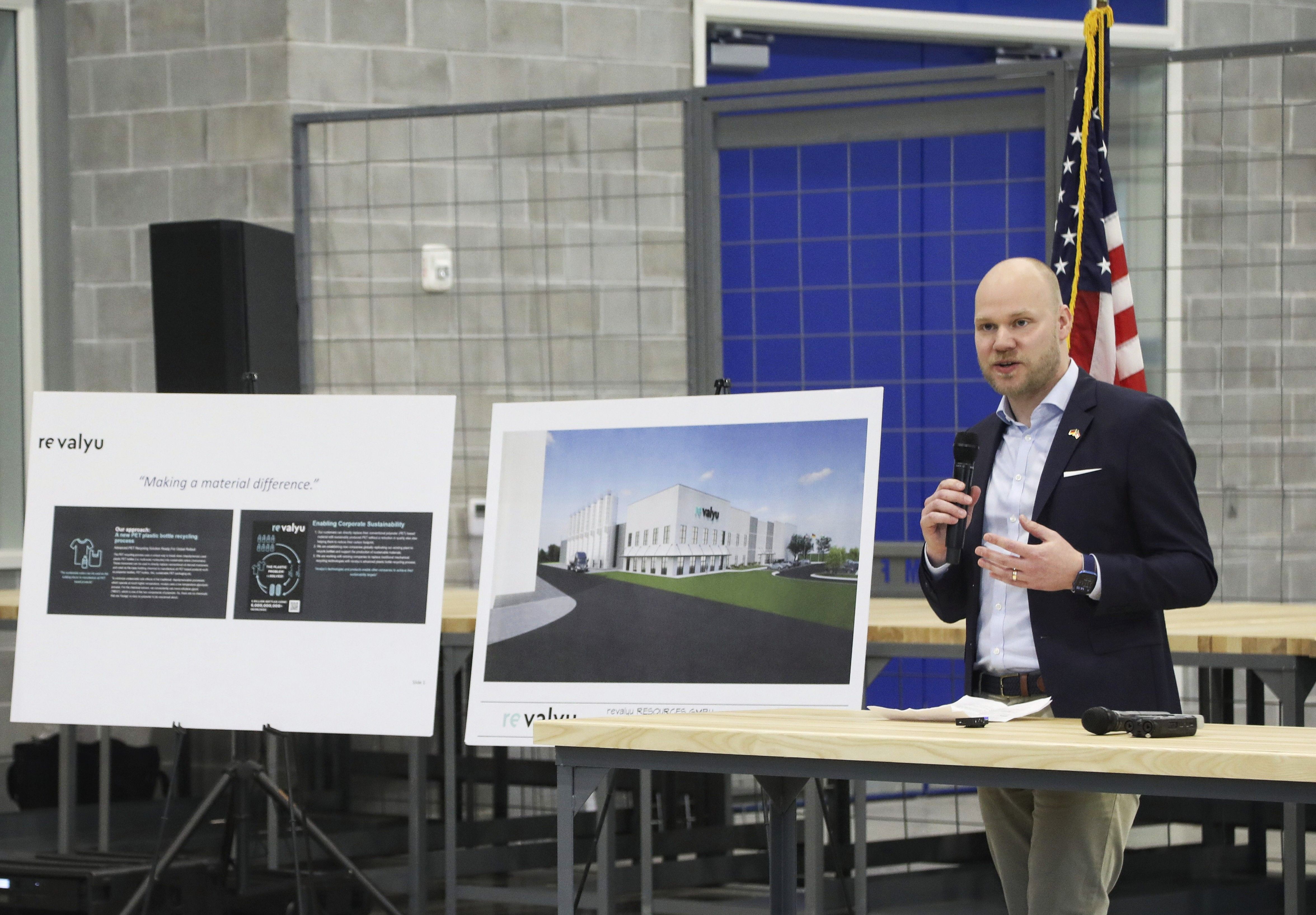 revalyu公司总经理Jan van Kisfeld拿着麦克风在两张海报旁讲话