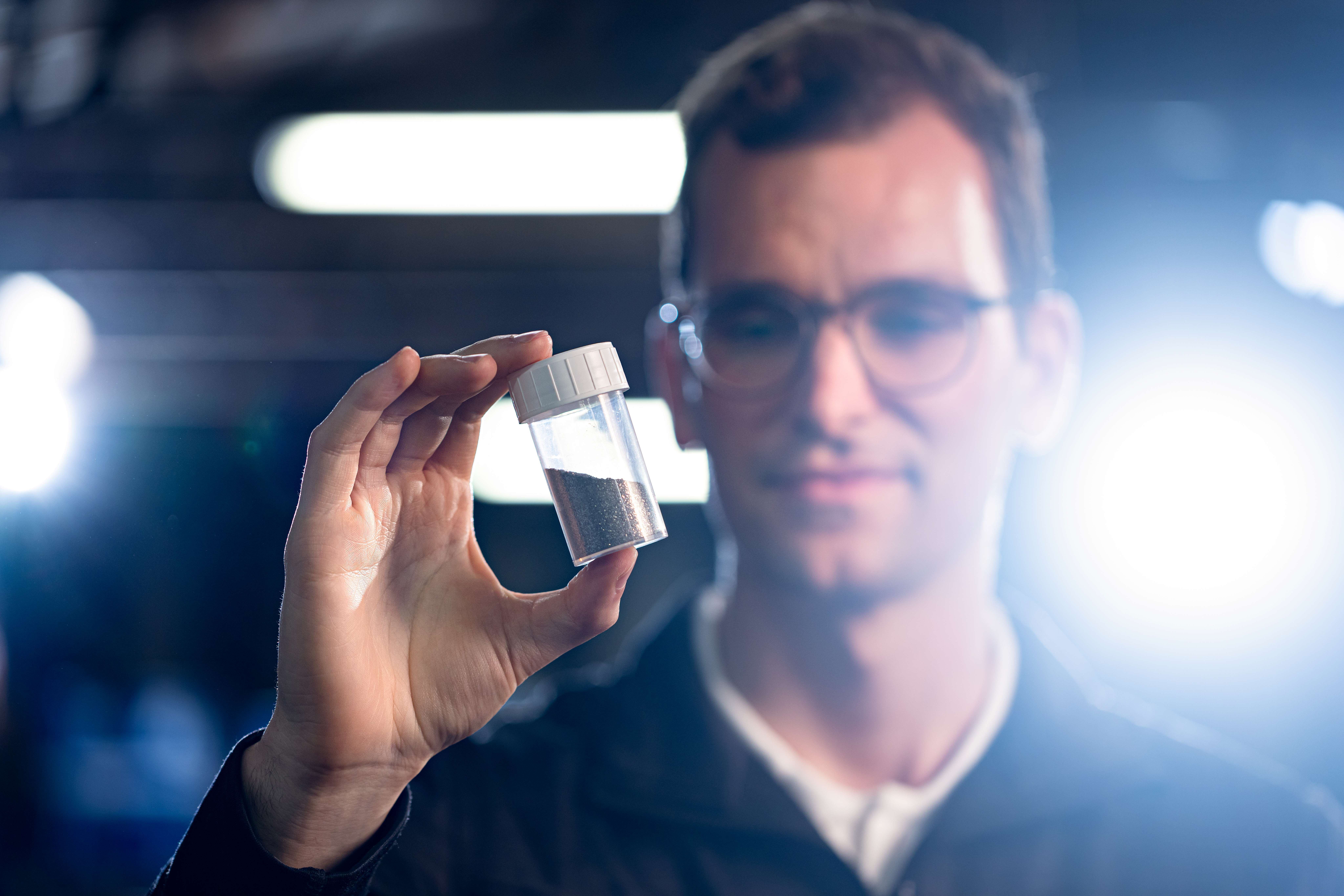 Heraeus Mitarbeiter zeigt recyceltes Magnetmaterial in einem Probenglas.