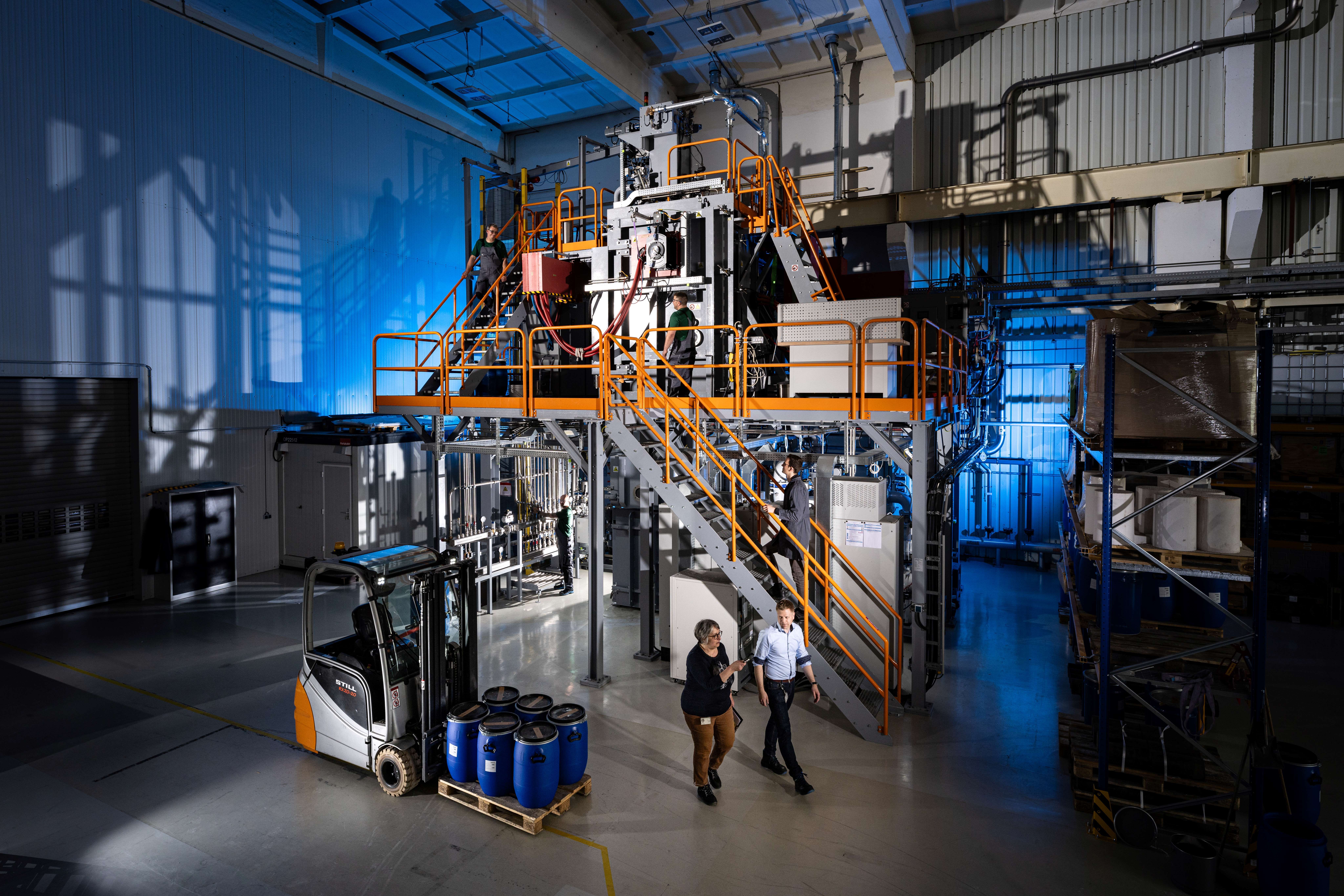 Mitarbeiter von Heraeus arbeiten an der Recycling-Anlage in Bitterfeld-Wolfen. Im Vordergrund steht ein Gabelstapler mit Materialfässern.